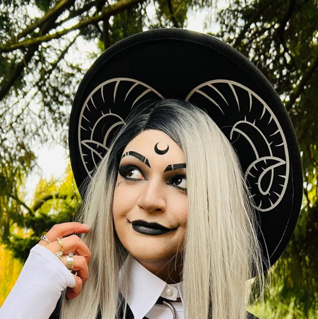 Person with white hair wearing a wide brim felt hat with curled goat horns design printed on the brim.