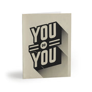 An off-white greeting card with large all-caps black text reading, "You do you".
