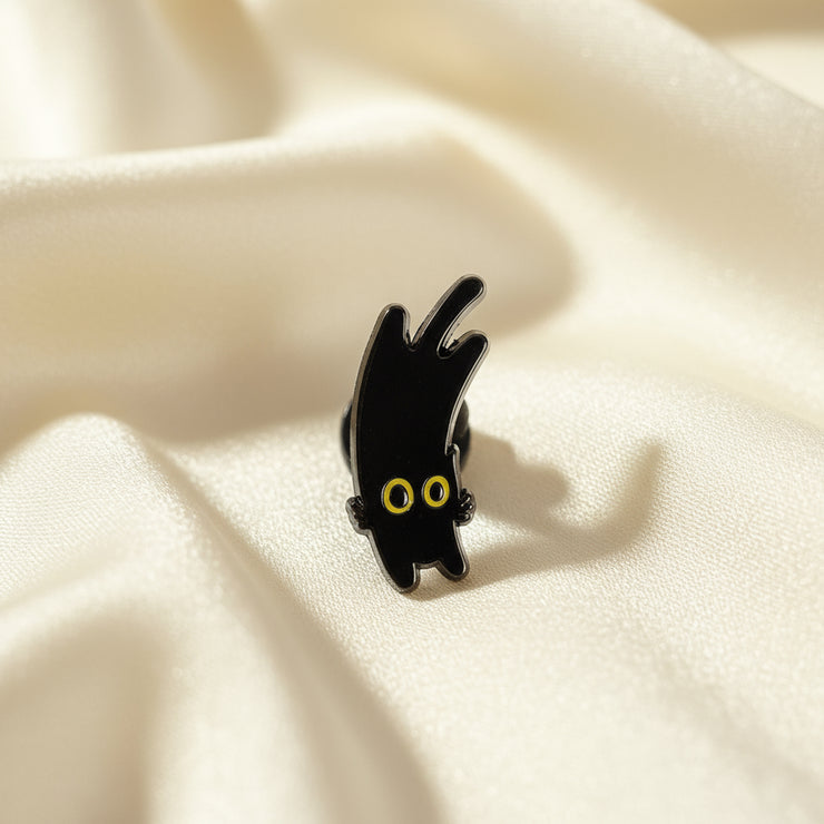 Black cat-shaped pin with yellow eyes on a white background