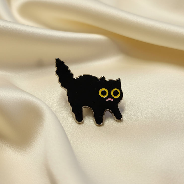 Black cat-shaped pin with yellow eyes and a pink mouth on a light fabric background