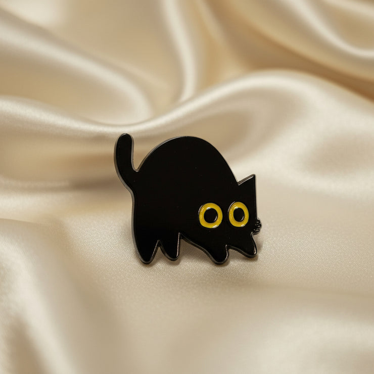 Black ghost-shaped pin with gold eyes on a light gray background