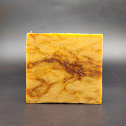 Square piece of marbled yellow and brown soap on a dark gray background
