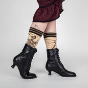 Person wearing black high-heeled boots and patterned knee-high socks with a white background