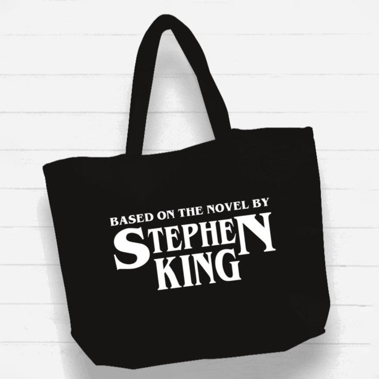 Black tote bag with 'Based on the Novel by Stephen King' text on a white wooden background