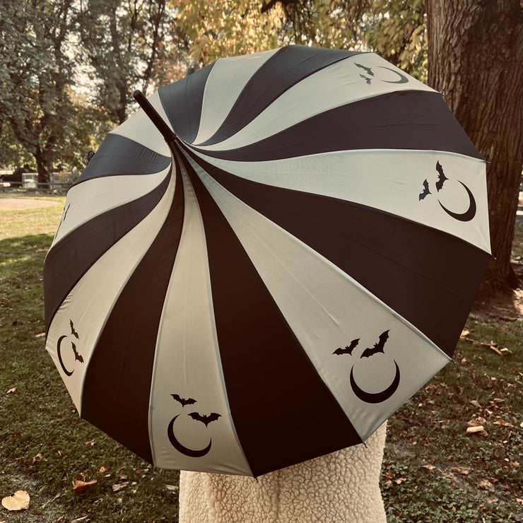Black and white striped umbrella with bat and moon designs held by a person in a park.