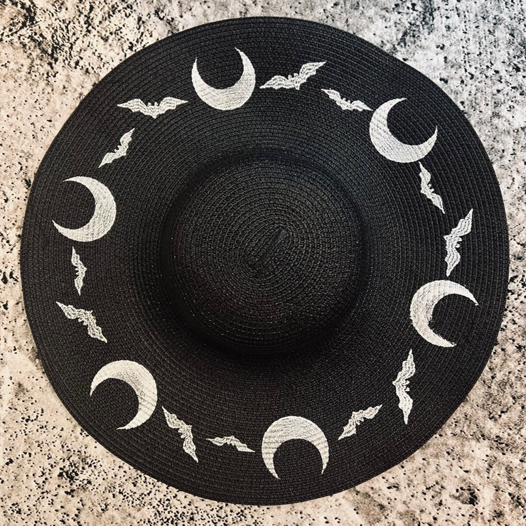 Black straw hat with white moon and bat designs on a textured surface