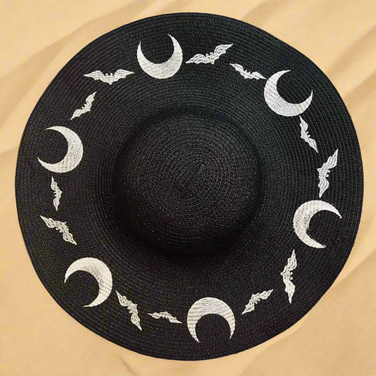 Black sun hat with white moon and bat designs on a beach sand background