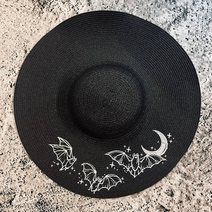 Black sun hat with bat and moon designs on a gray textured surface