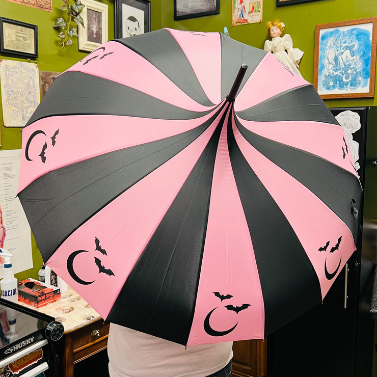Person holding a pink and black umbrella with moon and bat designs in a room with green walls and various items.