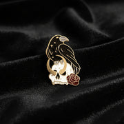 Enamel pin of a crow on a human skull with crescent moon and rose details on a dark background.