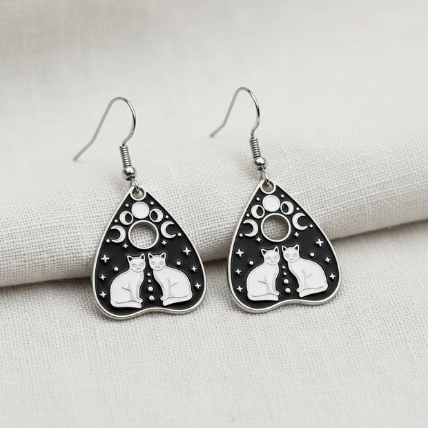 Planchette-shaped earrings with intricate black and white designs on a light gray background