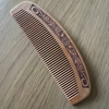 A curved wooden comb with fine teeth and an engraved floral scroll pattern, shown on a light wood grain surface.