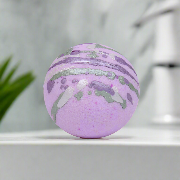 A purple bath bomb with gray and silver swirls on a marble bathroom countertop