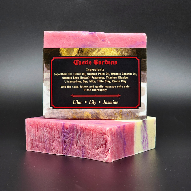 A labeled bar of pink, purple and white Castle Gardens Handmade Vegan Bar Soap on a dark background. Scent notes of Lilac Lily and Jasmine.