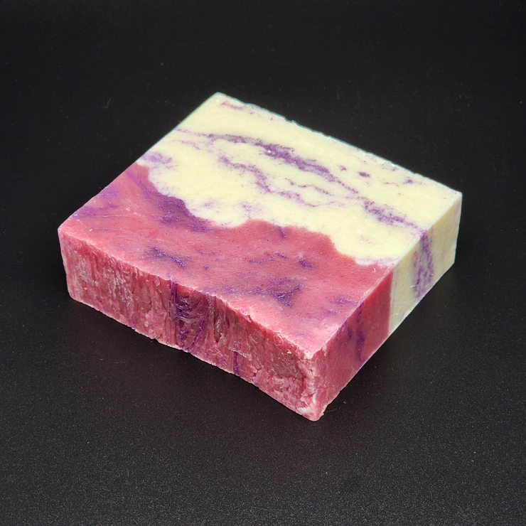 A bar of pink, purple and white Castle Gardens Handmade Vegan Bar Soap on a dark background. Scent notes of Lilac Lily and Jasmine.