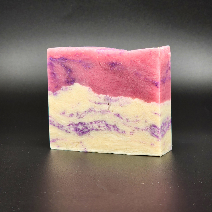 A bar of pink, purple and white Castle Gardens Handmade Vegan Bar Soap on a dark background. Scent notes of Lilac Lily and Jasmine.