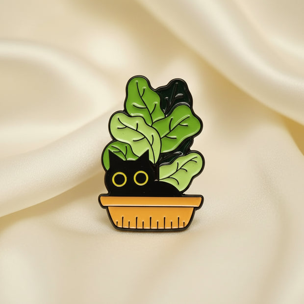 Enamel pin with green leaves and a yellow eyed cat on a beige background