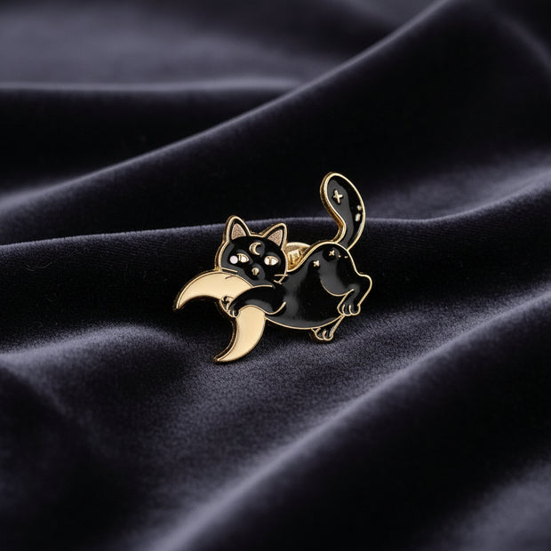 Black cat and moon enamel pin on a textured dark surface