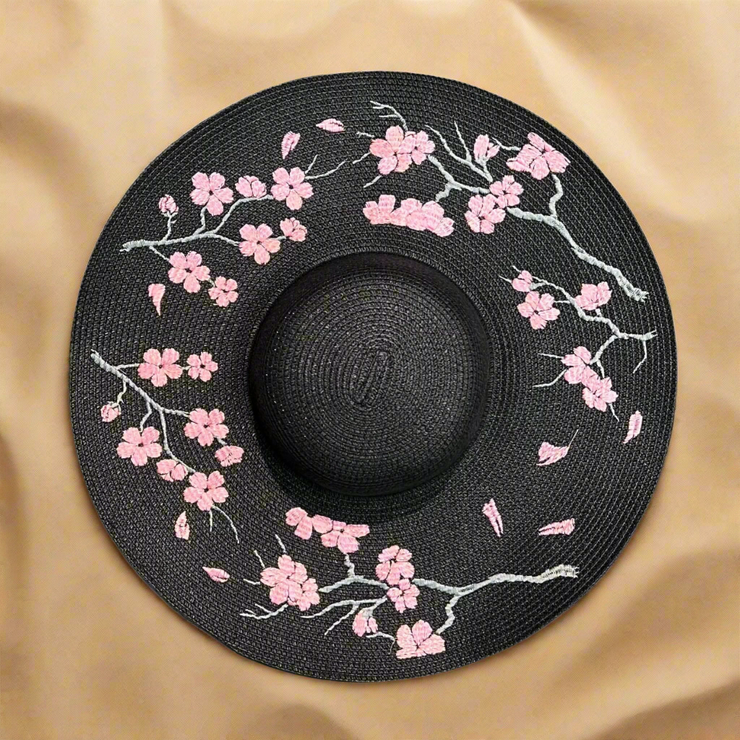 Black sun hat with pink floral embroidery on a beach sand background