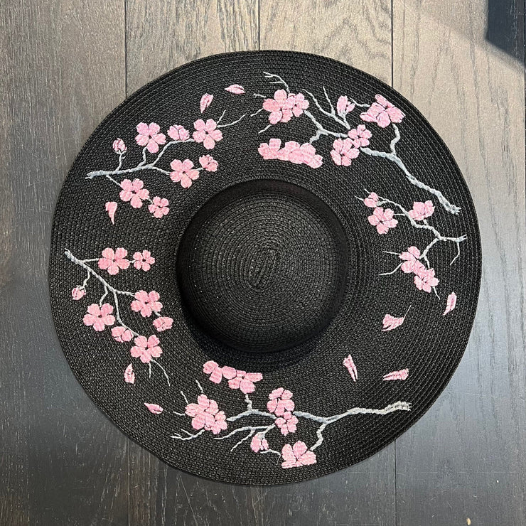 Black sun hat with pink floral design on a wooden surface