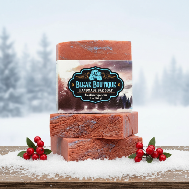 Two bars of Bleak Boutique handmade soap stacked on a snowy surface with berries and a blurred winter background.