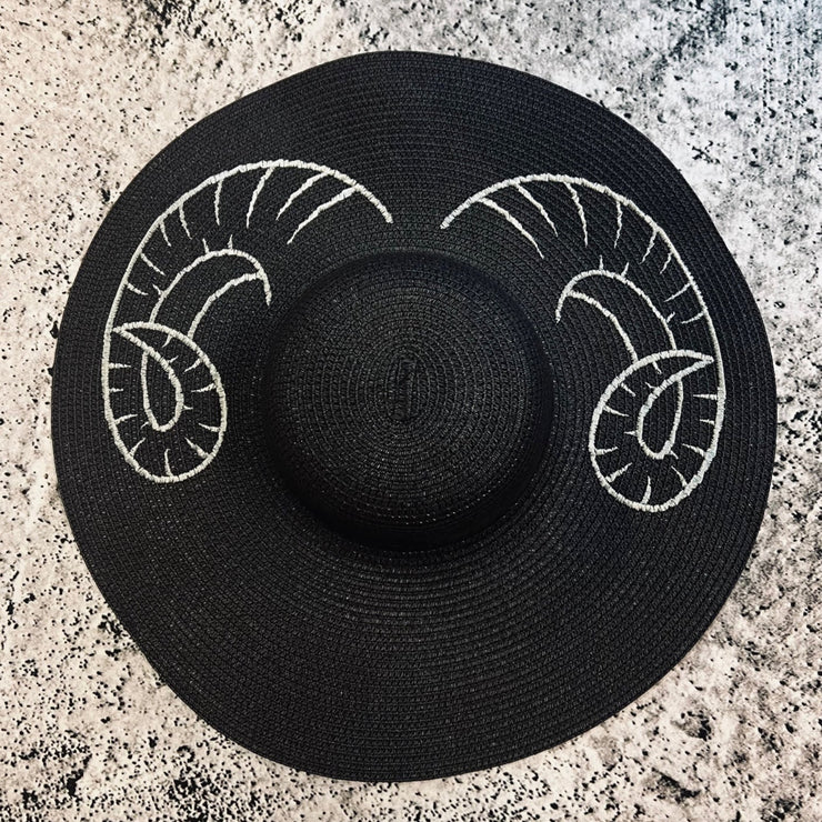 Black straw hat with white ram horns design on a textured surface