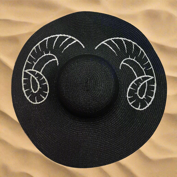 Black hat with white ram horns design on a beige sand background