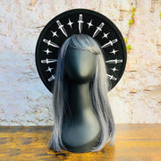 Mannequin head with gray wig on a stone surface with a black hat brim featuring white dagger and star symbols.