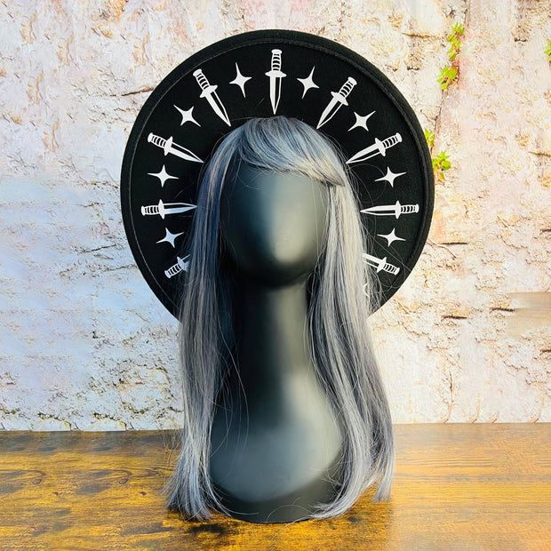 Mannequin head with gray wig on a stone surface with a black hat brim featuring white dagger and star symbols.