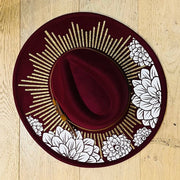 Red hat with gold and white floral design on a wooden surface