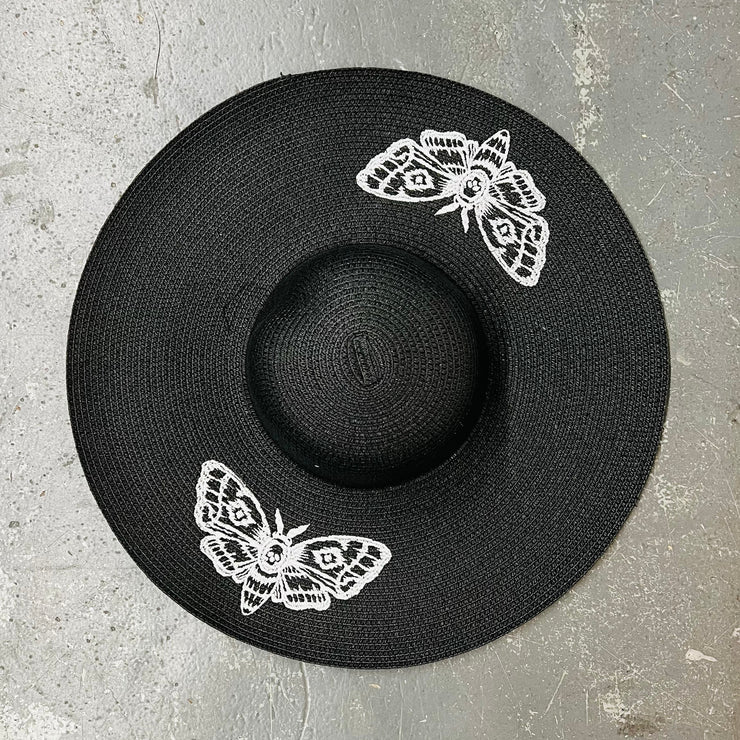 Black hat with white moth designs on a gray surface