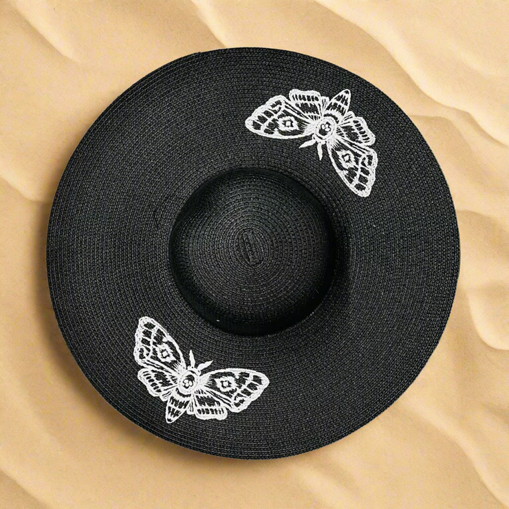 Black hat with white moth designs on a beach sand background