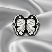 An enamel pin depicting a split open skull revealing a butterfly within on a light colored background