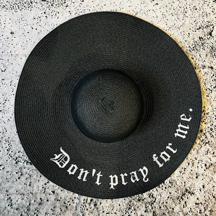 Black straw hat with 'Don't pray for me.' text on a gray textured surface