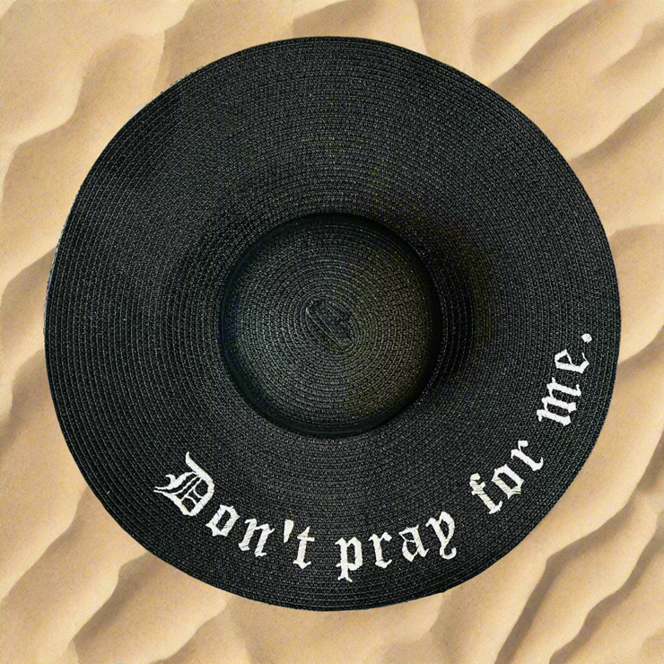 Black straw hat with 'Don't pray for me' text on a beach sand background