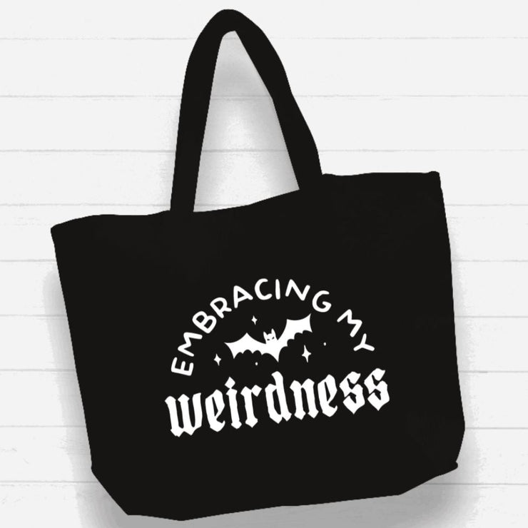 Black tote bag with 'Embracing my weirdness' text and bat design on a white background