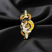 An enamel pin of a snake wrapped around a dagger and skull on a dark background.