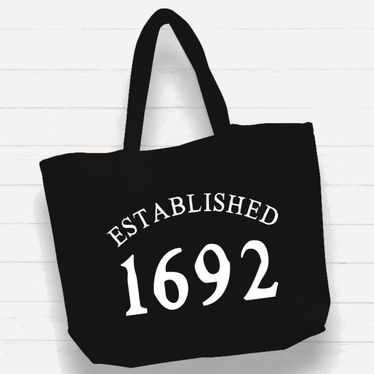 Black tote bag with 'ESTABLISHED 1692' text on a white wooden background