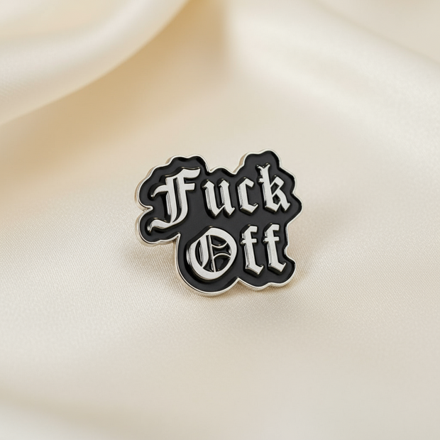Black and white 'Fuck Off' enamel pin on a beige background