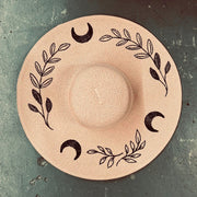 Blush pink straw hat with black leaf and moon designs on a textured surface