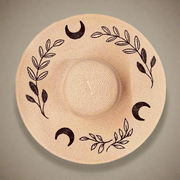 Blush pink straw hat with black moon and leaf patterns on a beige background