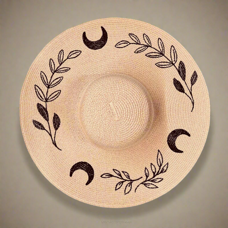 Blush pink straw hat with black moon and leaf patterns on a beige background