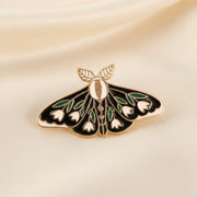 Decorative butterfly pin with gold, green, and white details on a dark background