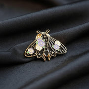 Decorative butterfly enamel pin with gemstones on a dark textured surface