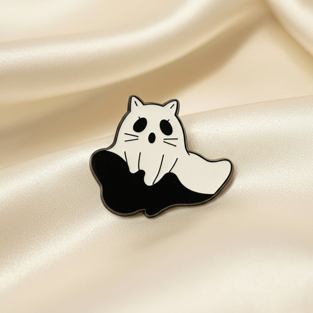 An enamel pin shaped like a ghost with cat ears and whiskers on a light background