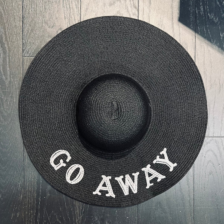 Black straw hat with 'GO AWAY' text on a wooden surface