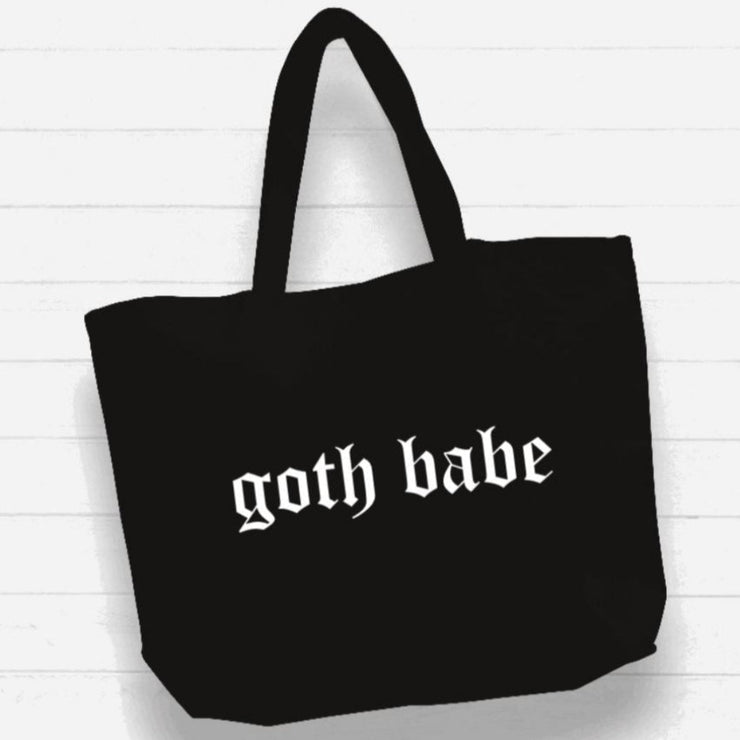 Black tote bag with 'goth babe' text on a white wooden background
