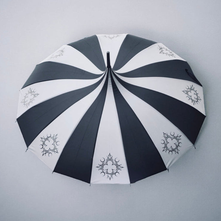 Black and white striped umbrella with decorative quatrefoil patterns on a gray background