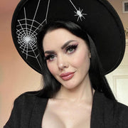 Woman wearing a black hat with spider web and spider design, against a neutral background.