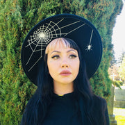 Person wearing a black hat with spider web design outdoors.